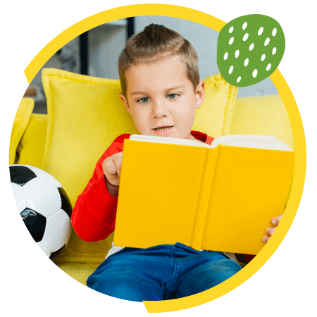 A little boy sitting on the sofa and reading a book
