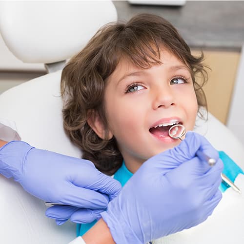 A little boy with opened mouth lying in a white dental chair and wearing a white dental bib during a procedure